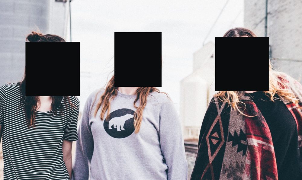 Three friends photographed beside a railway line, each face covered by a solid black bar